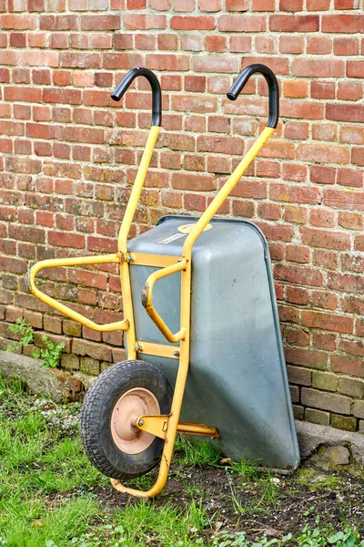 Wheelbarrow against the side of a red brick wall or house. Doing gardening or cleanup work in a backyard garden on a sunny day. Professional landscapers use this equipment to move soil or dirt.