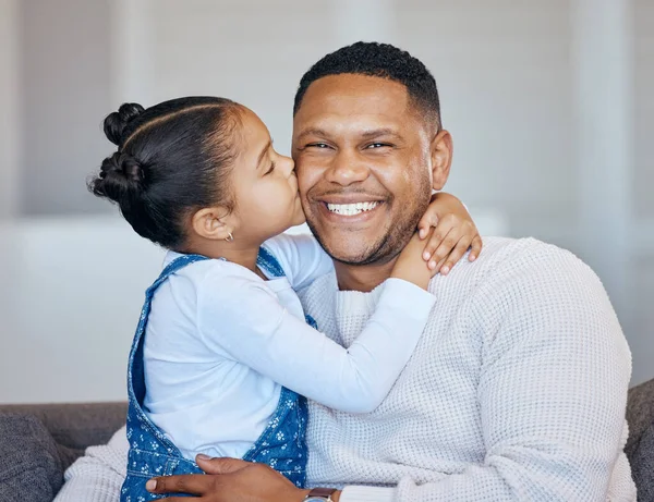 Adorable little girl kissing her dad on the cheek. African american man laughing and looking joyful while receiving love and affection from his daughter. Man being spoiled on fathers day.