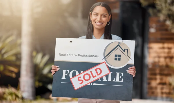Shot of a real estate agent standing next to a sold sign outside.