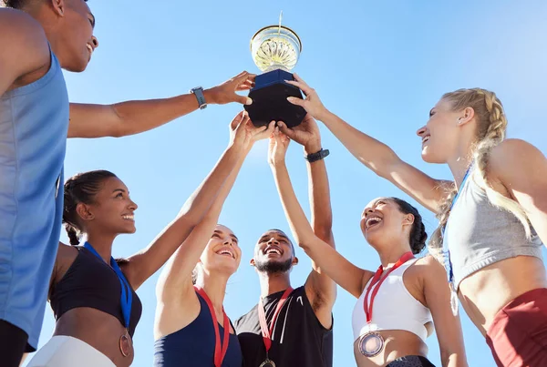 A diverse team of athletes celebrating a victory with a golden trophy and looking excited. A fit and happy team of professional athletes rejoicing after winning an award at an athletic sports event.