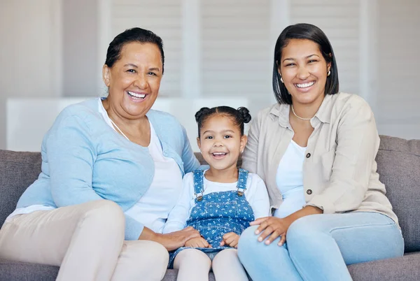 Happy mature grandmother relaxing with her granddaughter and adult daughter at home. Cheerful little hispanic girl sitting on the couch together with her mother and grandmother.