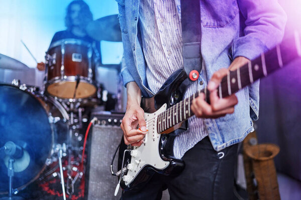 Cropped shot of an unrecognizable male guitarist performing on stage with his bandmates in the background.