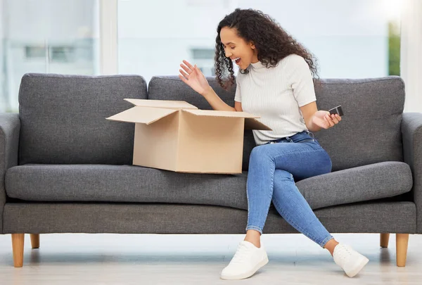 Shot of a young woman opening a box on the couch at home.