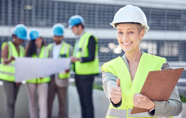 Cropped portrait of an attractive female construction worker giving thumbs up while standing on a building site with her colleagues in the background.