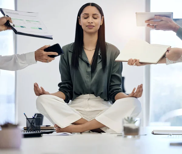 Shot of a young businesswoman meditating on a desk in a demanding work environment.