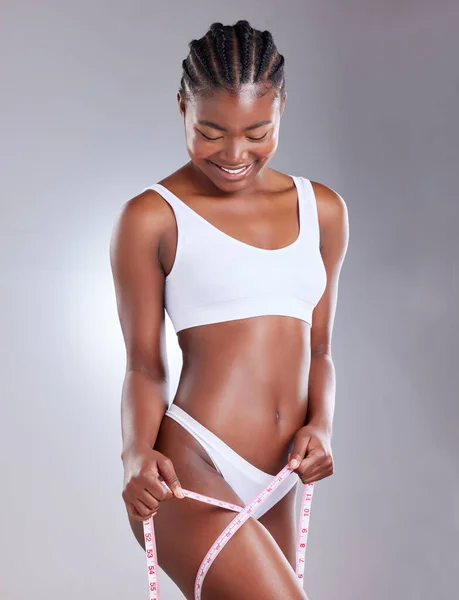 Shot of a woman measuring her thigh with tape measure against a studio background.