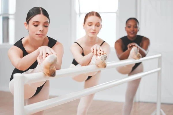 Shot of a group of ballet dancers leaning against a barre.