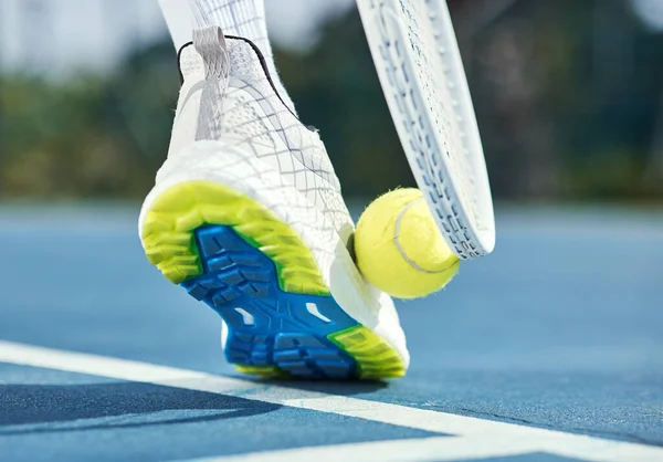 Cropped shot of an unrecognisable man using his foot and racket to pick up a tennis ball during practice.