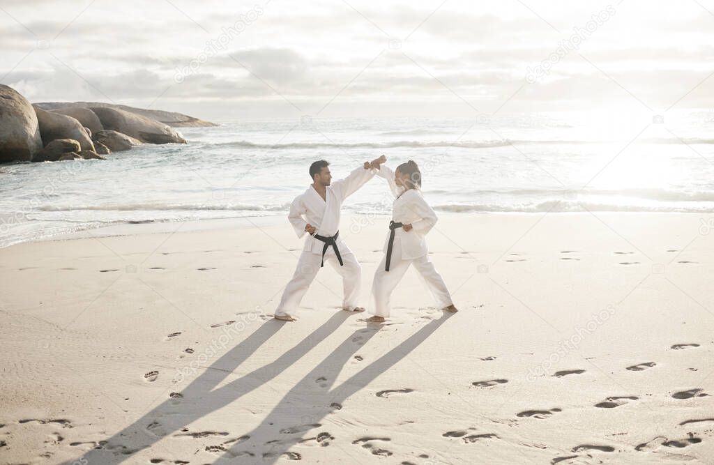Full length shot of two young martial artists practicing karate on the beach.