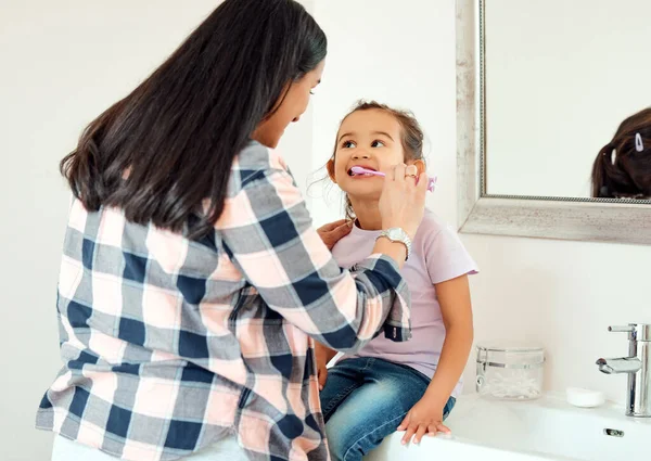 Shot of a mother helping her little daughter brush her teeth in the bathroom at home.