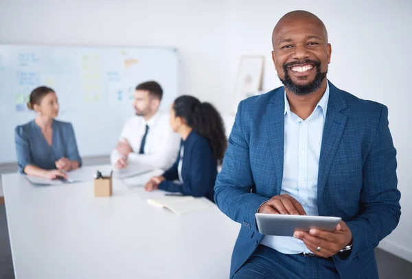 Portrait of smiling confident african american businessman in boardroom using digital tablet. Diverse group of businesspeople in meeting and working behind black manager. Browsing online on technology