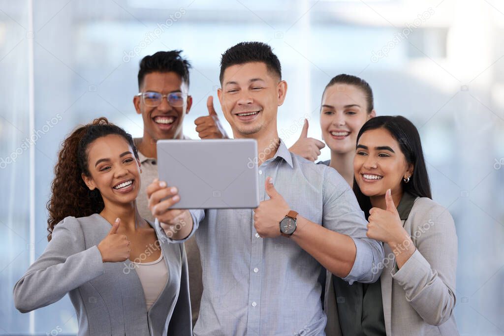 Shot of a group of young businesspeople taking selfies with a digital tablet and showing thumbs up in a modern office.