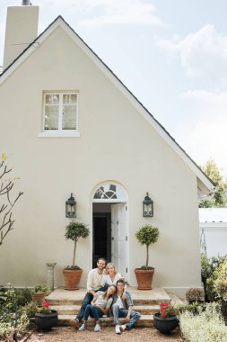 Shot of a couple and their two children sitting in front of their house.