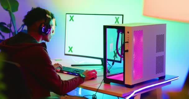 绿色屏幕的电脑游戏玩家晚上戴着耳机 在家里的卧室里玩扑克游戏 青少年男孩坐在黑暗的房间里 用一个复制的空间桌上型显示器来做运动或虚拟运动 — 图库视频影像