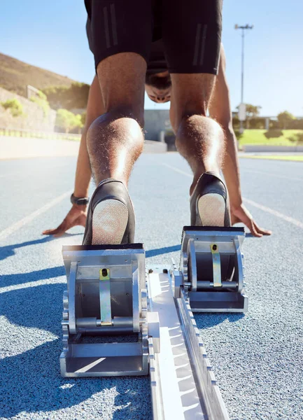 Feet of athlete in starting position on a running track. A male track and field runner ready to leave the starting block to start his sprint. Sportsman with hands on the starting line during a race.
