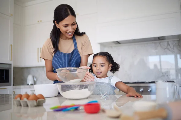 Single mother teaching daughter baking skills and bonding together in home kitchen. Cute little girl learning cooking with her smiling mom. Happy parent showing curious child how to sieve flour.