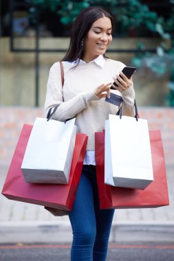 a woman using her cellphone while walking outside with shopping bags.
