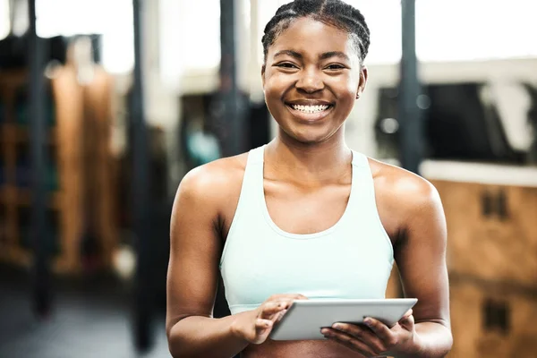 an attractive young woman standing alone in the gym and using a digital tablet.