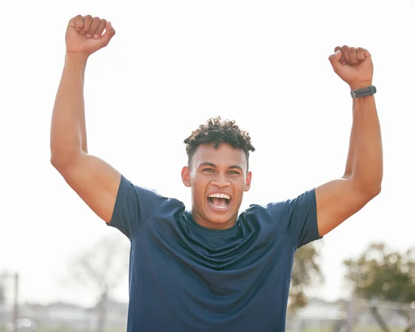 Cropped portrait of a handsome young male athlete standing outside with his hands in the air.