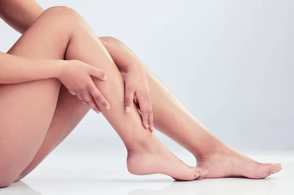 an unrecognisable woman sitting alone in the studio and touching her legs.