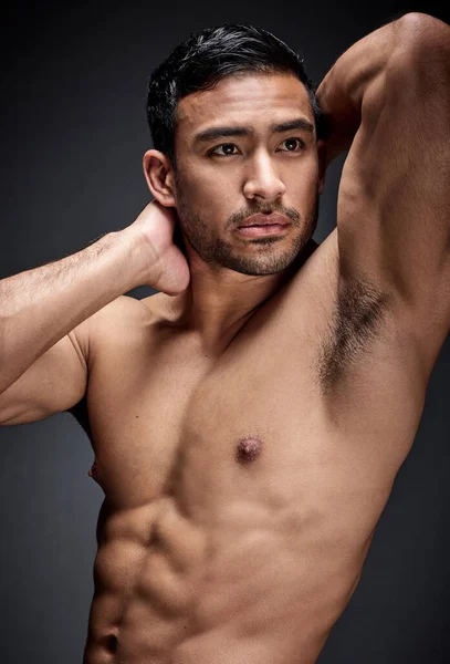 a handsome young man standing alone and posing shirtless in the studio.