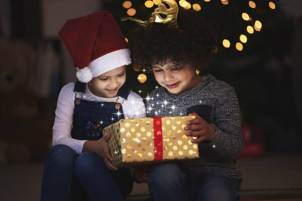 two little siblings opening up a gift together at home.