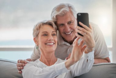 an affectionate senior couple taking selfies while relaxing in the living room at home.