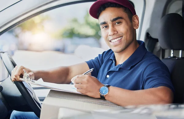 Portrait of a young delivery man writing on a clipboard while sitting in a van.