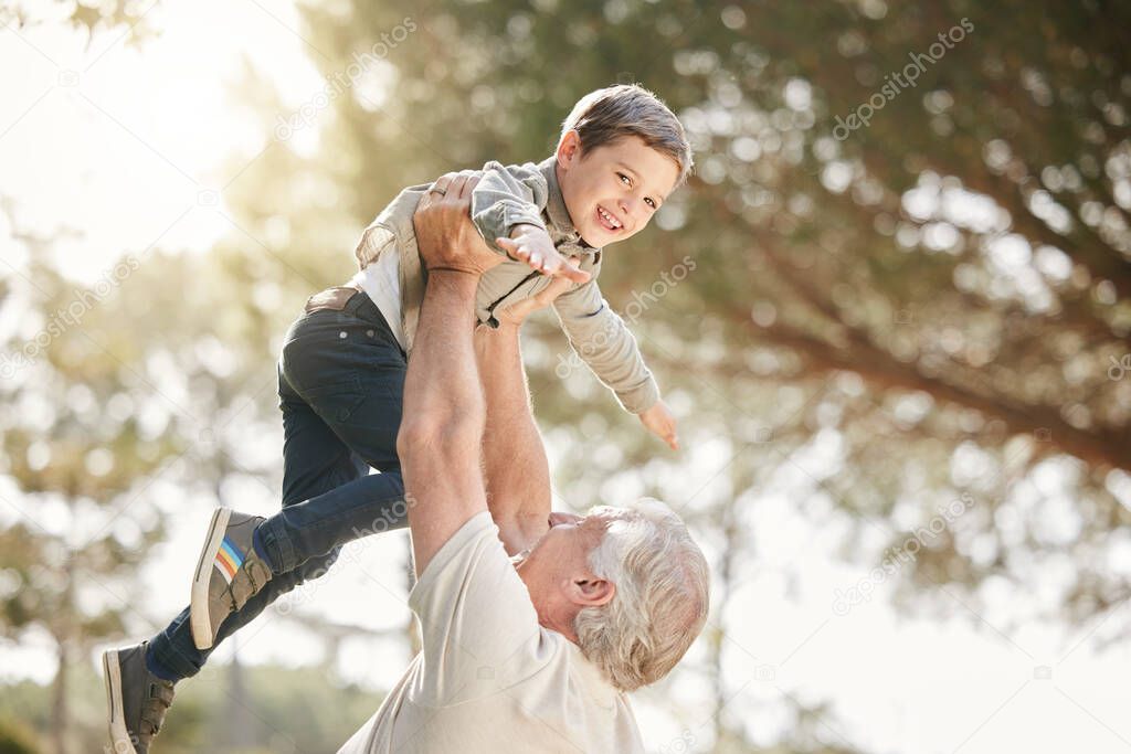 Excited little caucasian boy having fun with his grandfather as he lifts him up while playing outdoors. Active senior man playing with energetic grandson at park.