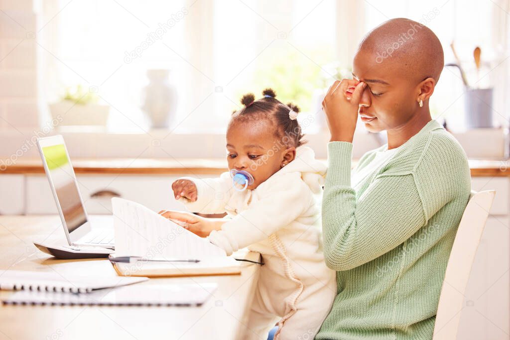 a young mother looking stressed while holding her baby and working from home.