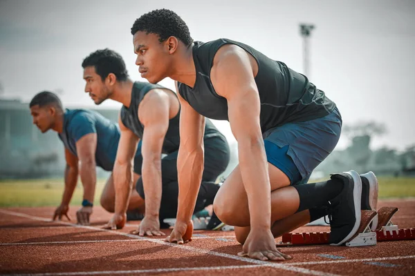 Full length shot of three handsome young male athletes starting their race on a track.