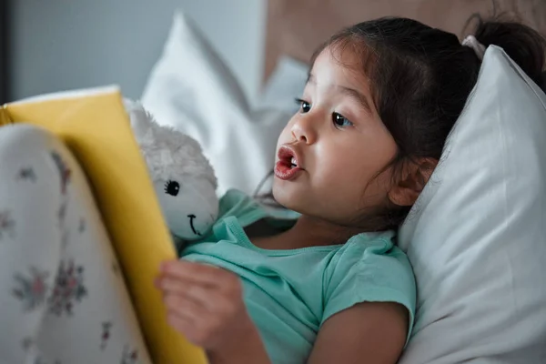 Little Girl Reading Book While Lying Her Bed — Stock fotografie