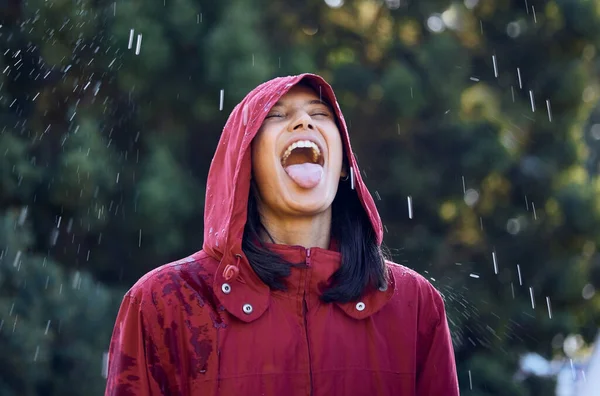 a young woman sticking out her tongue to feel the rain outside.