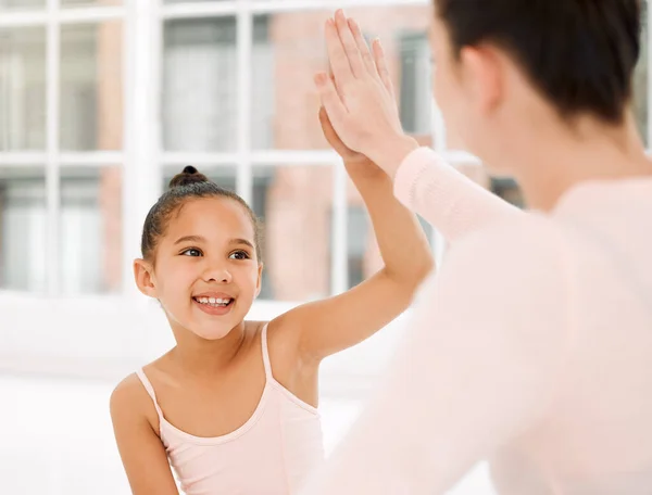 a young ballerina and her teacher celebrating with a high five in a dance studio.