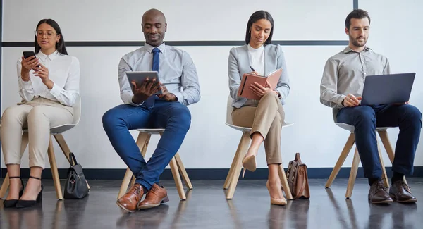 a group of businesspeople using different forms of technology while waiting in line at an office.