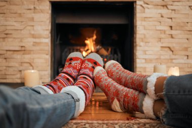 Closeup shot of a couple wearing Christmas socks while relaxing with their feet up by a fireplace at home.