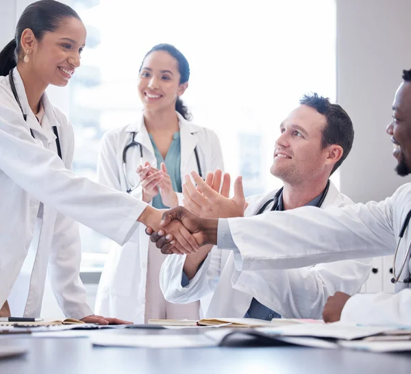 a group of doctors applauding as a new team member is welcomed aboard during a meeting.