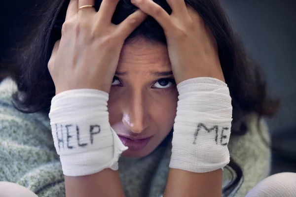 a young woman with bandages wrapped around her wrists showing help written on them.