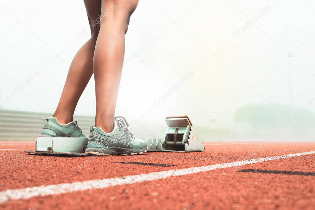 an unrecognizable sportswoman standing next to starting blocks on a running track.
