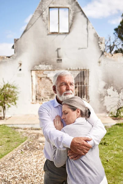 a senior couple comforting each other after losing their home to a fire.