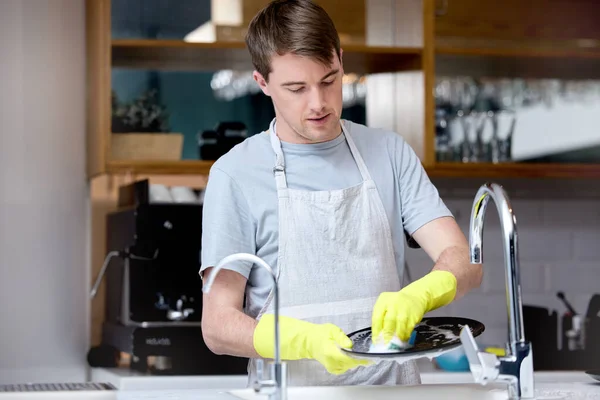 a young man washing dishes in his kitchen.
