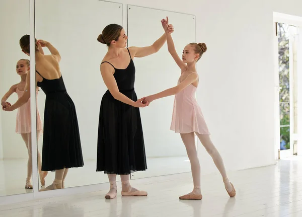 a young girl practicing ballet with her teacher in a dance studio.