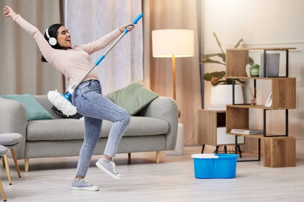 a young woman listening to music and dancing while mopping the floors at home.