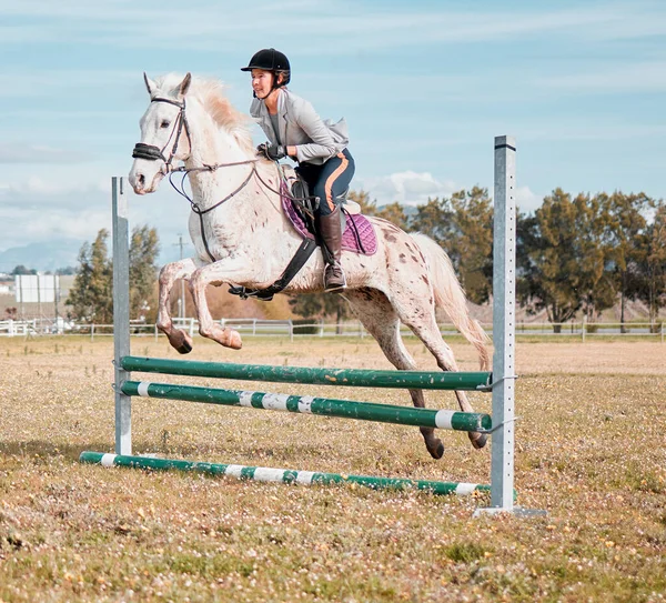 Há uma mulher montando um cavalo pulando sobre um obstáculo