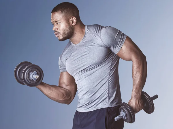 a handsome young man standing alone in the studio and using dumbbells during his workout.