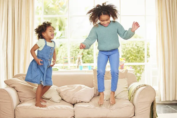 Full length shot of two adorable girls jumping on the sofa in the living room at home.