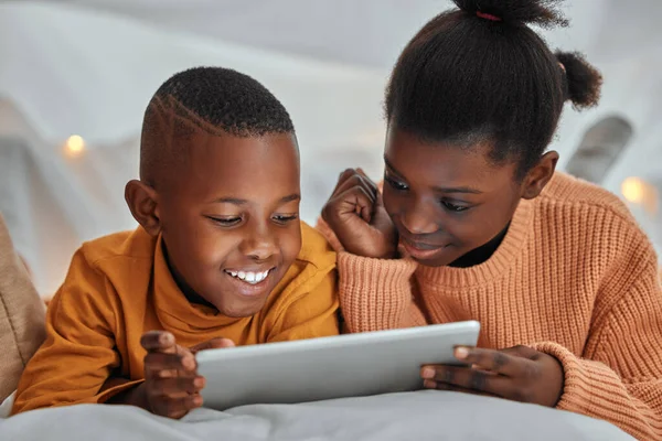 a brother and sister using a digital tablet together at home.