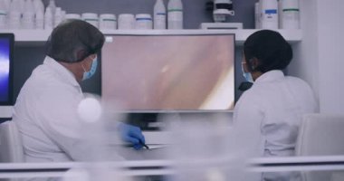 Modern bir araştırma laboratuvarında bilgisayar ekranındaki hücrelere bakan iki bilim adamı. Biyologlar, organizmalardaki bakterilerin mikroskobik görüntülerini bir monitörde analiz ediyor ve bulgularını tartışıyorlar..