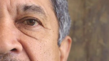 Closeup portrait of a senior mans eye at the optometrist. Side of a retired males face with zoom on his eyeball and lens. Staring and blinking at a checkup or test for infection of the conjunctiva.