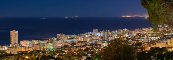 Copy space with dark night sky over the view of a coastal city seen from Signal Hill in Cape Town, South Africa. Calm and scenic panoramic landscape of lights illuminating an urban skyline by the sea.